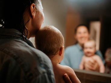 Kvinna med blöttt hår håller bebis i famnen i ett badrum